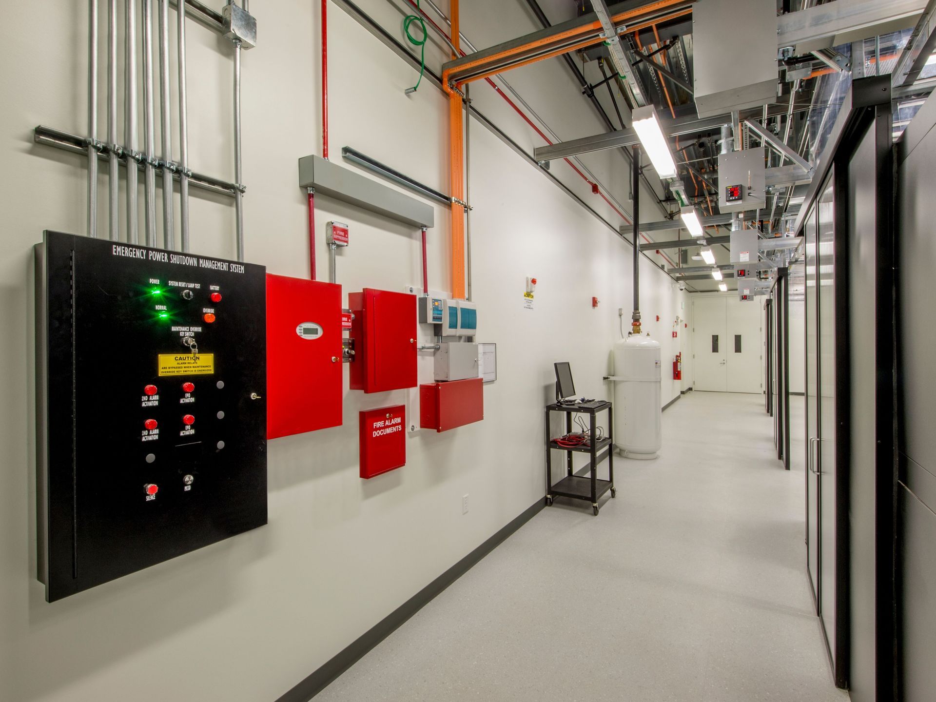 A hallway in a building with a lot of electrical equipment on the wall.