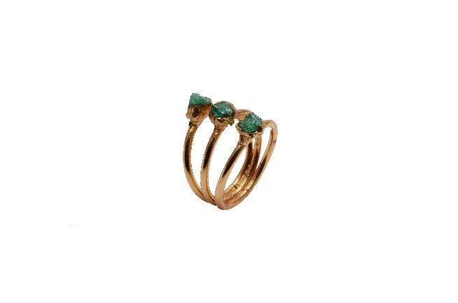 Un anillo de oro con tres piedras verdes sobre fondo blanco.