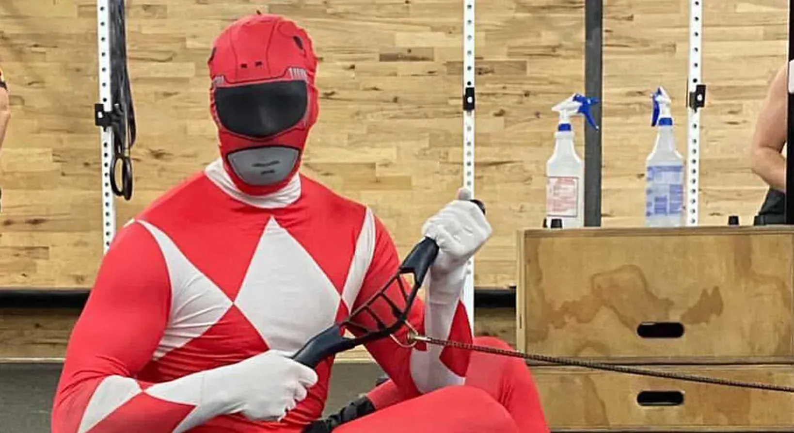 Red Power Ranger in a gym, seated, pulling on a cable machine.