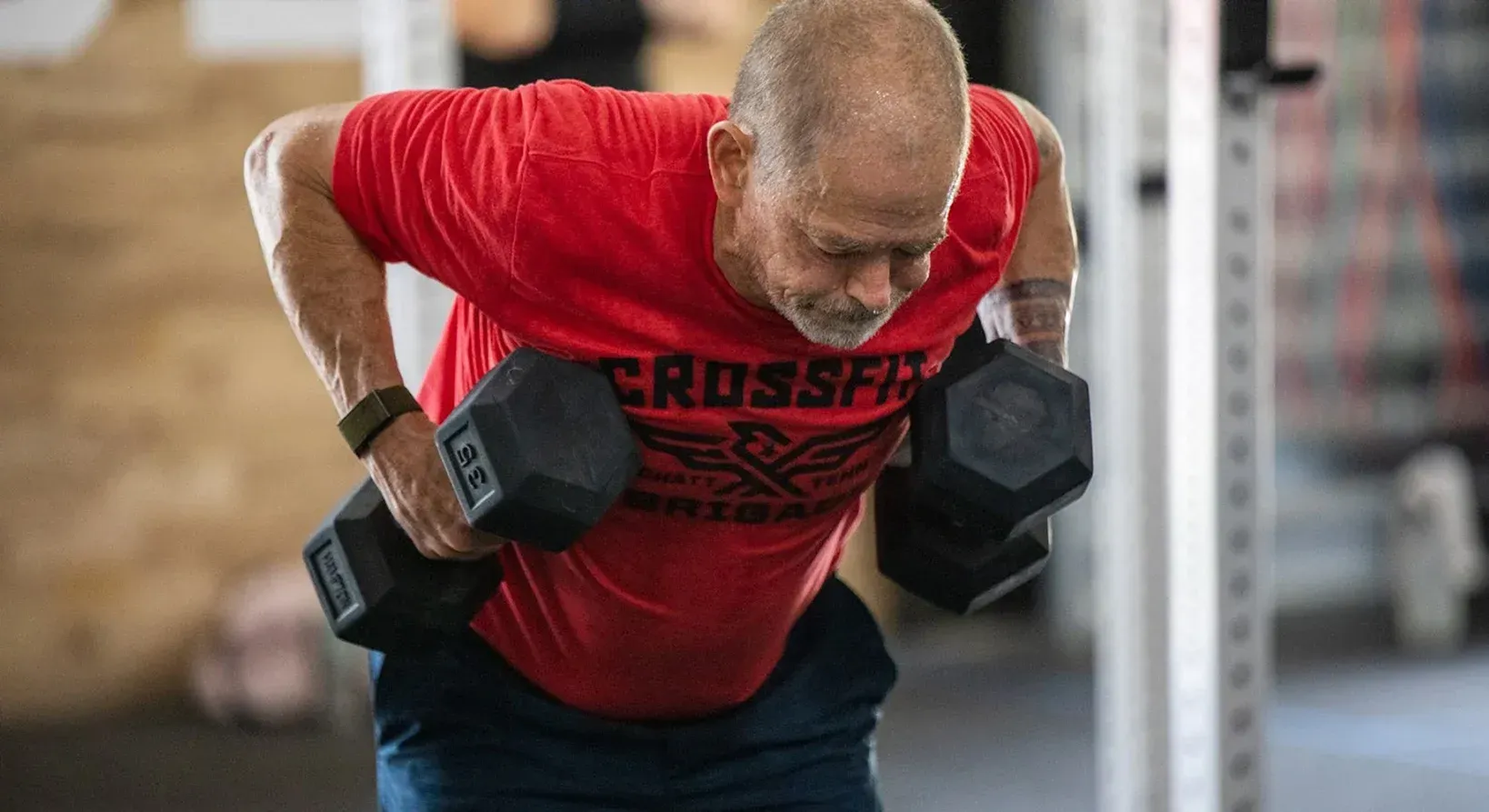 Man in red shirt doing dumbbell rows in at Brigade Athletic Club in Chattanooga.