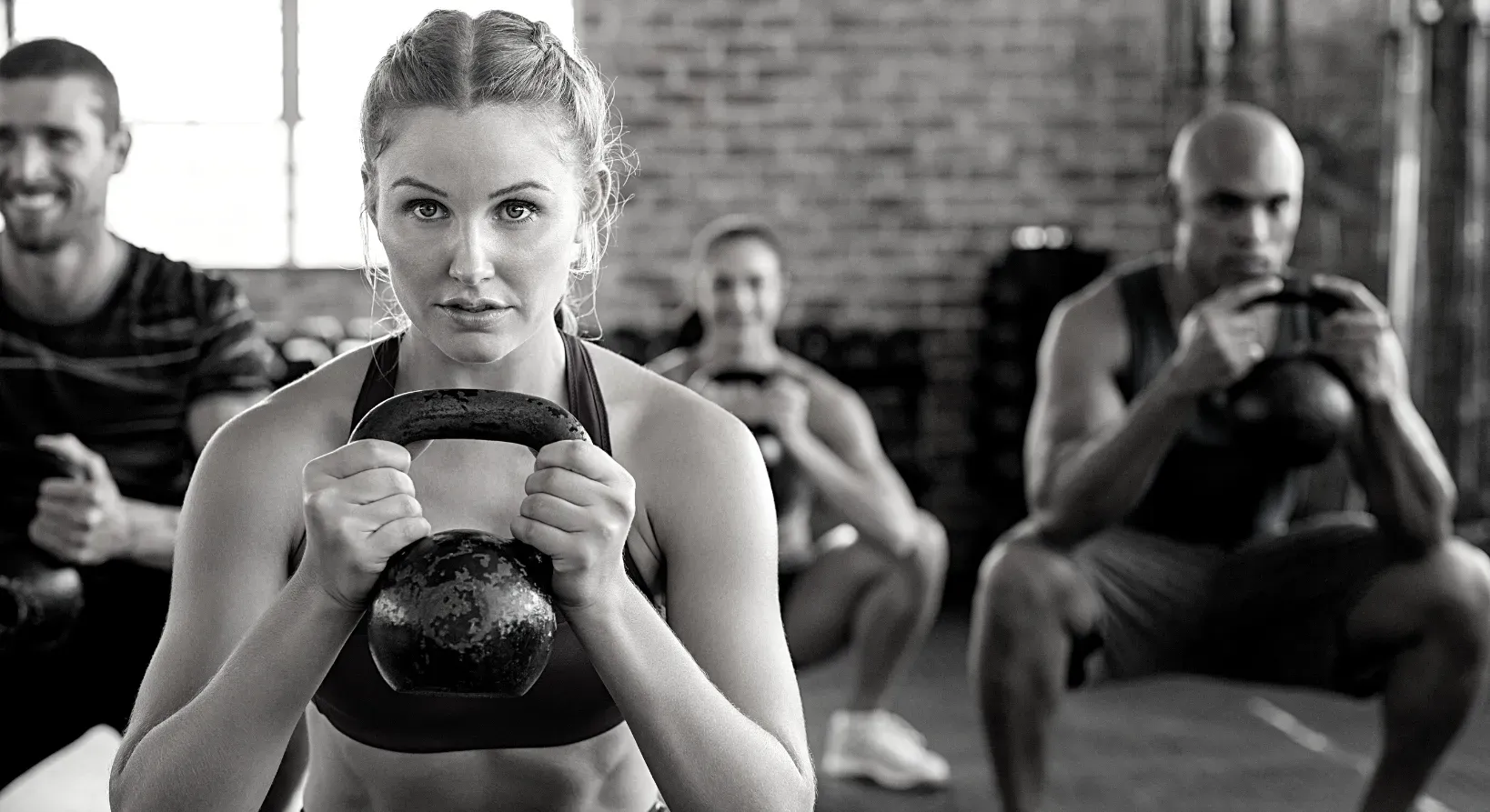 People in a gym, squatting and holding kettlebells.