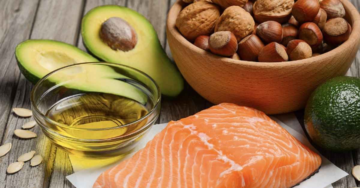 Avocado, salmon, nuts, and oil on a wooden table, representing healthy fats.