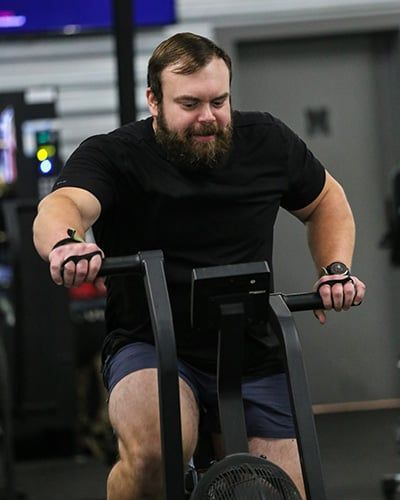 Man exercising on an air bike at Brigade Athletic Club in Chattanooga, wearing a black shirt and shorts.
