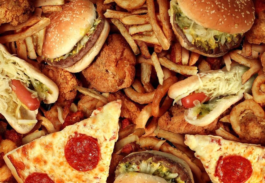 Pile of fast food: burgers, fries, pizza, hot dogs, fried chicken, and onion rings.