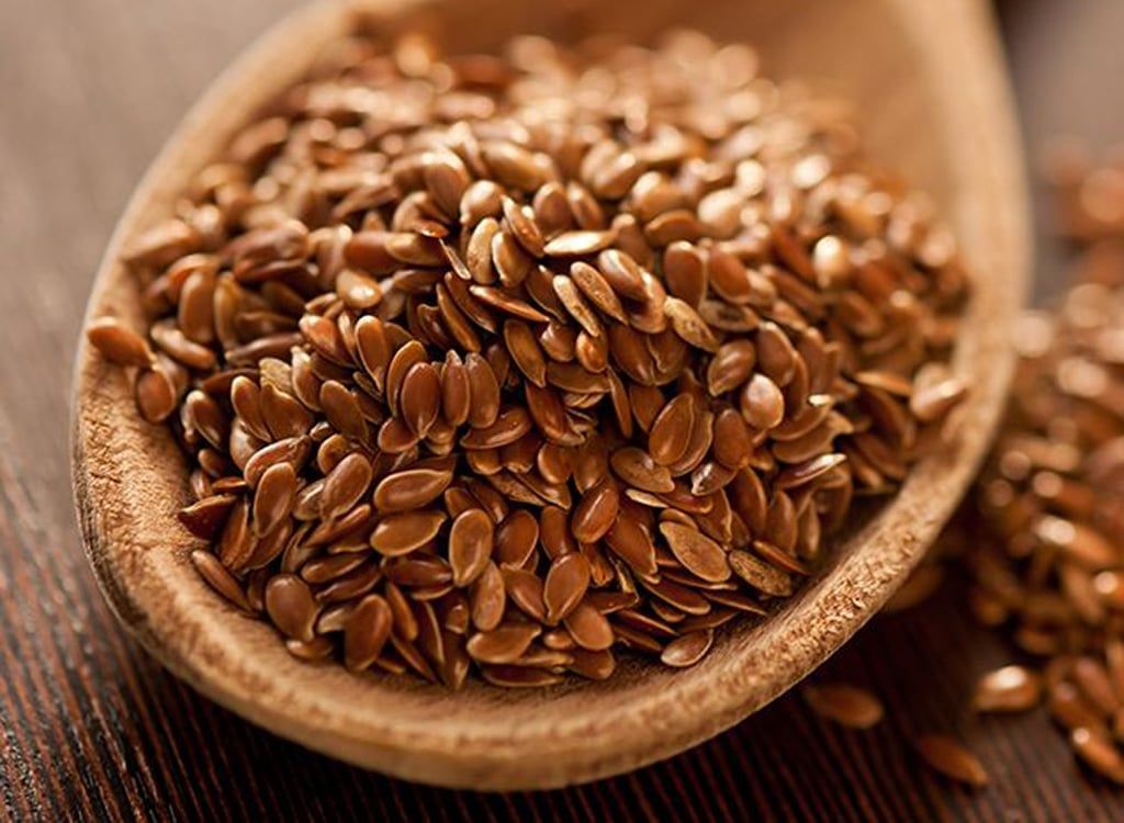 Brown flax seeds in a wooden spoon, close-up on a dark wooden surface.