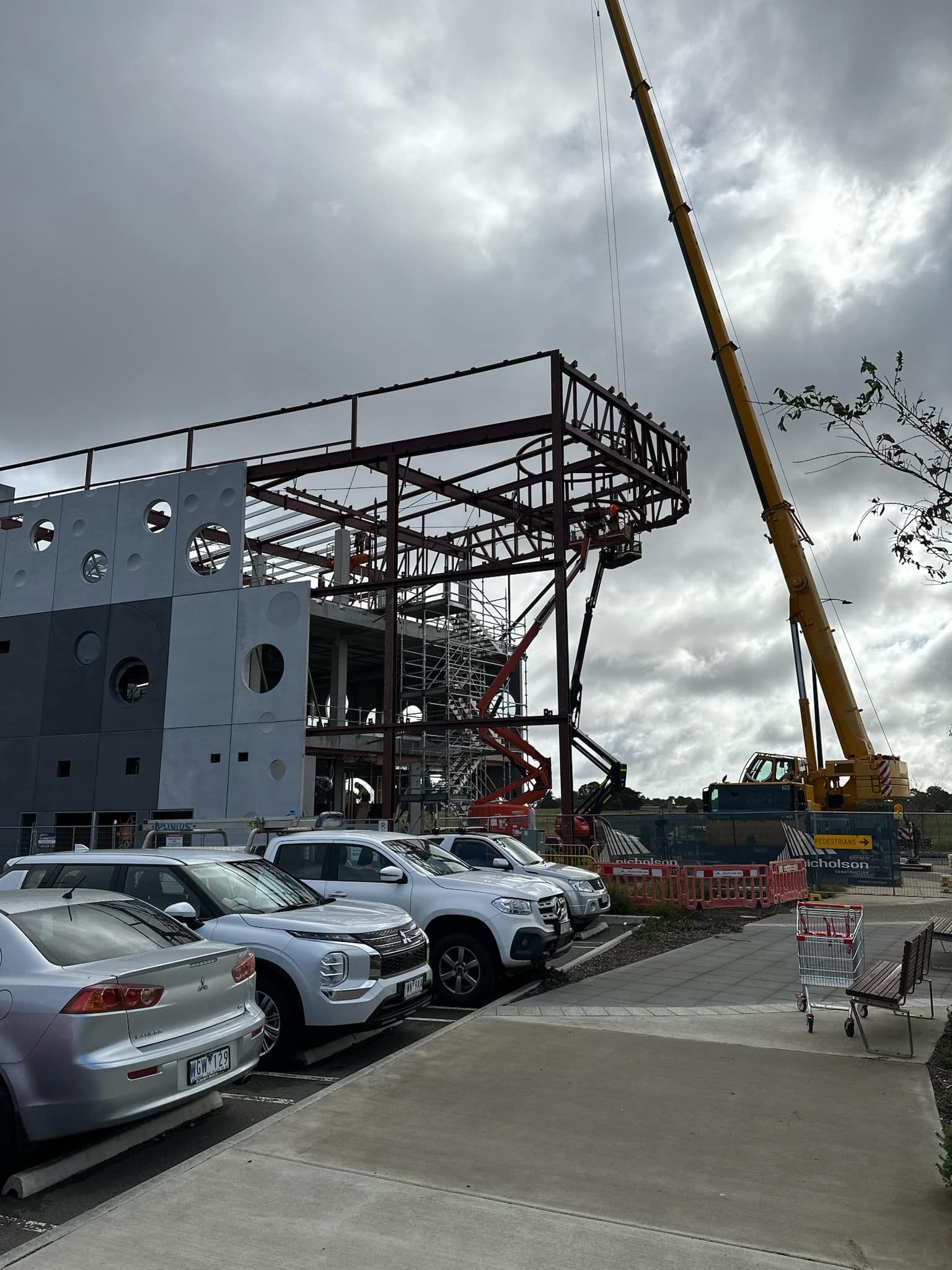 A row of cars are parked in front of a building under construction.