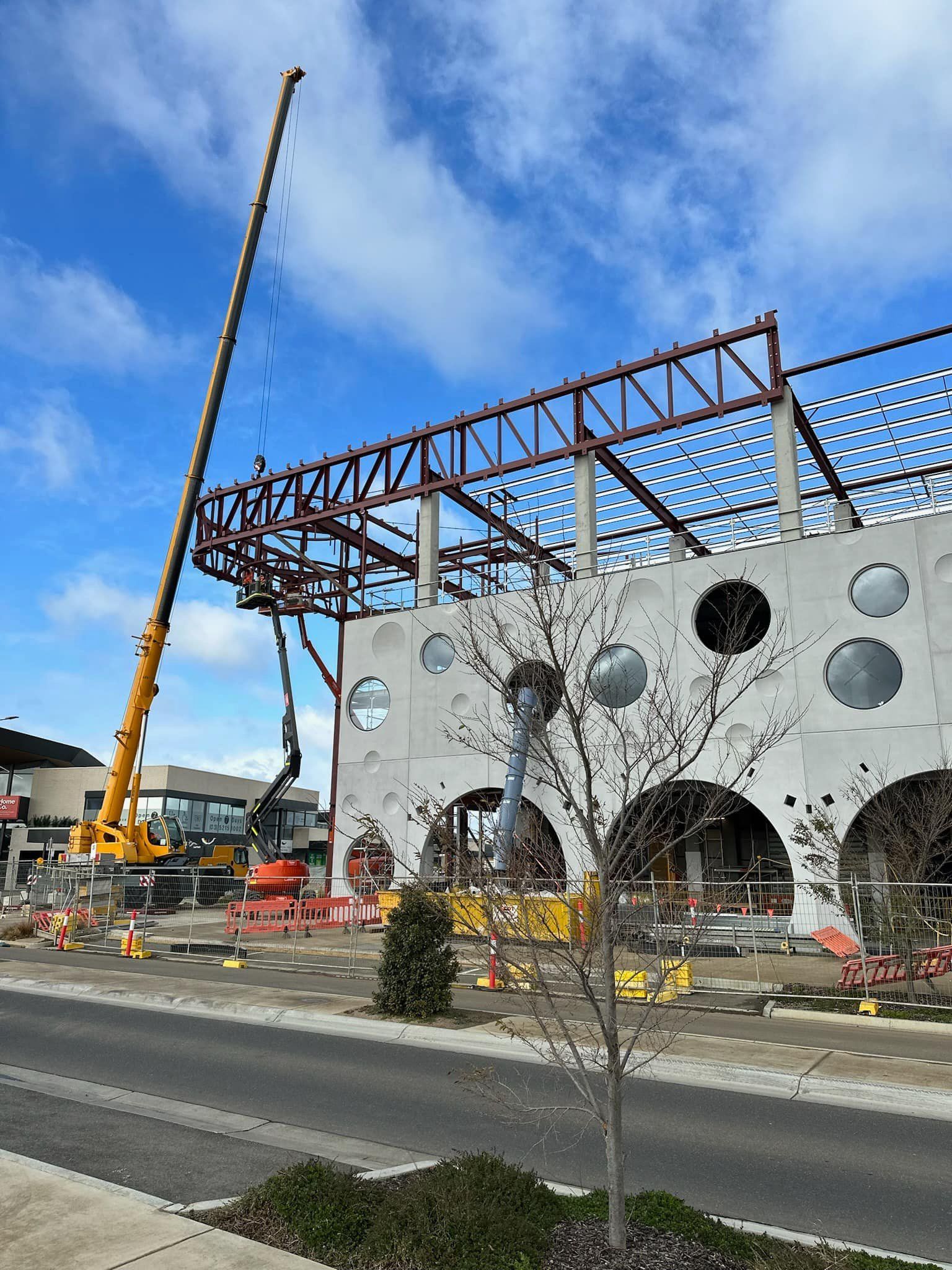 A large crane is lifting a metal structure over a building under construction.