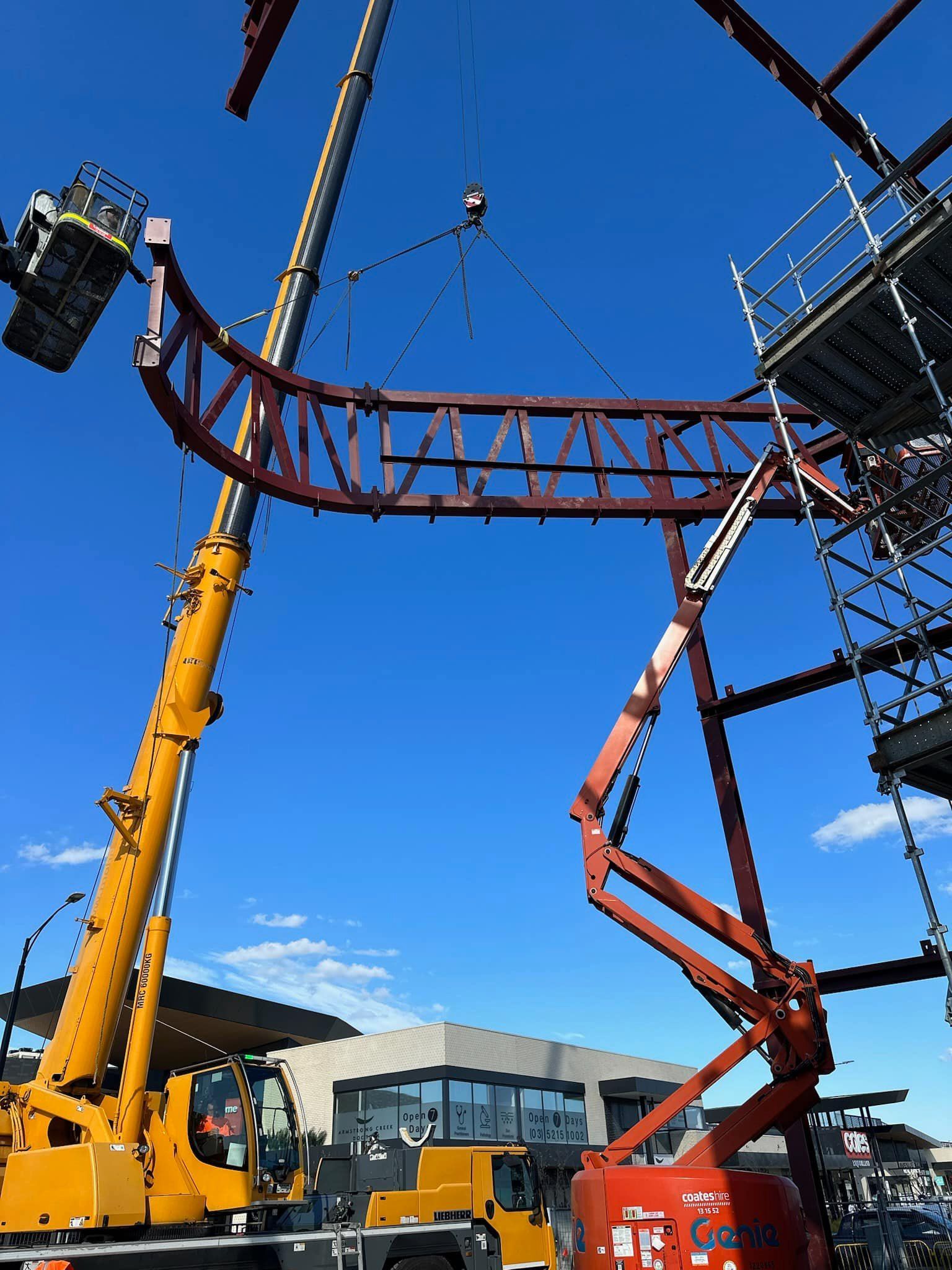 A yellow crane is lifting a large metal structure