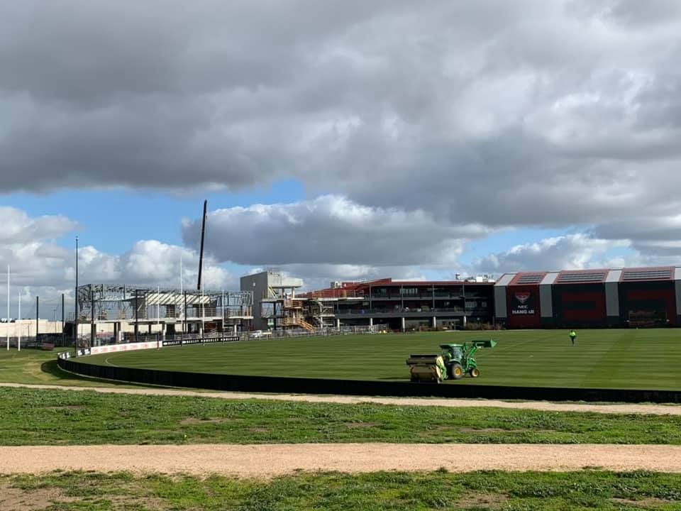 A tractor is cutting grass on a baseball field in front of a building.