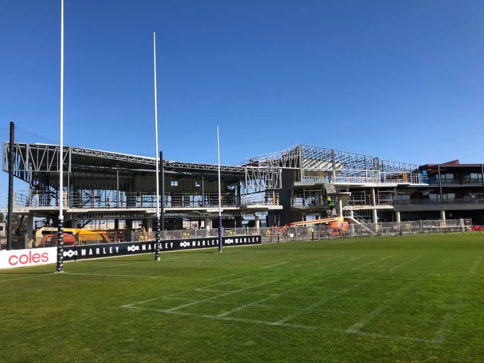 A large building is being built next to a soccer field.