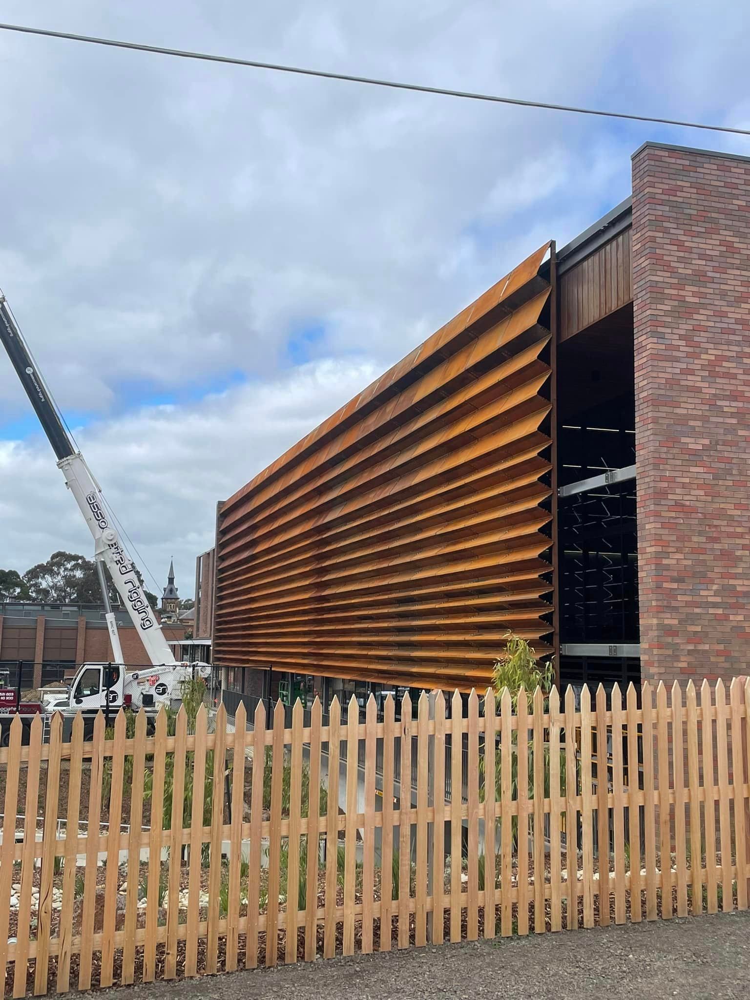 A wooden fence is in front of a brick building with a crane in the background.