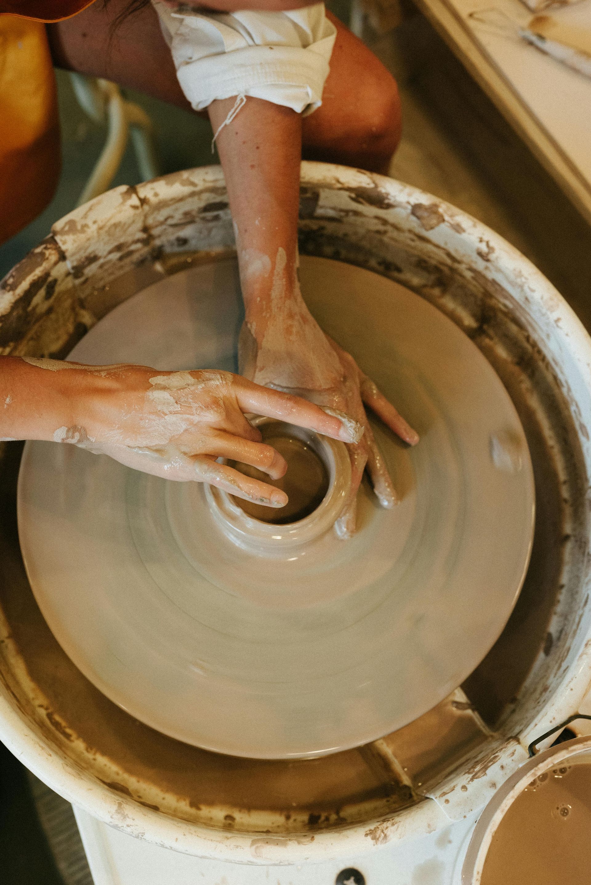Hands shaping clay on a spinning pottery wheel.
