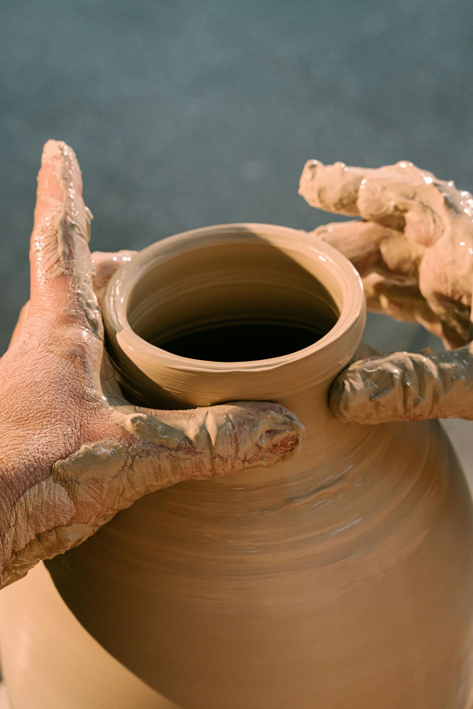 Hands shaping a clay pot on a potter's wheel, close-up.