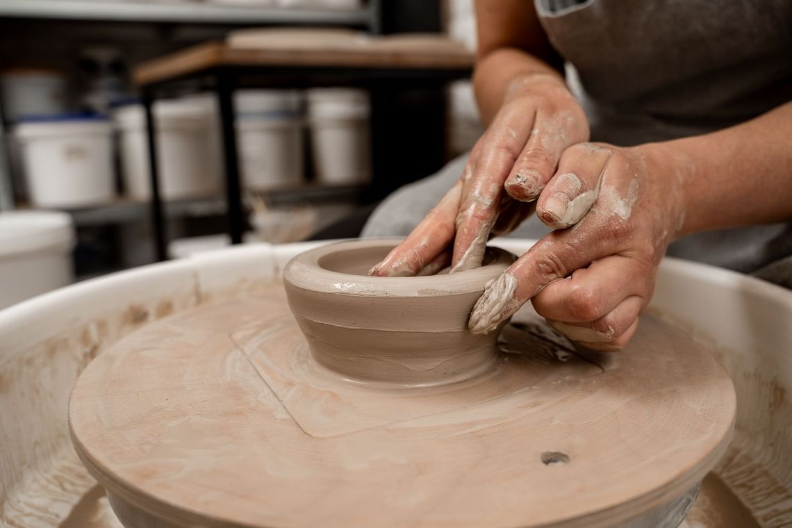 Person shaping clay bowl on a pottery wheel in a workshop.