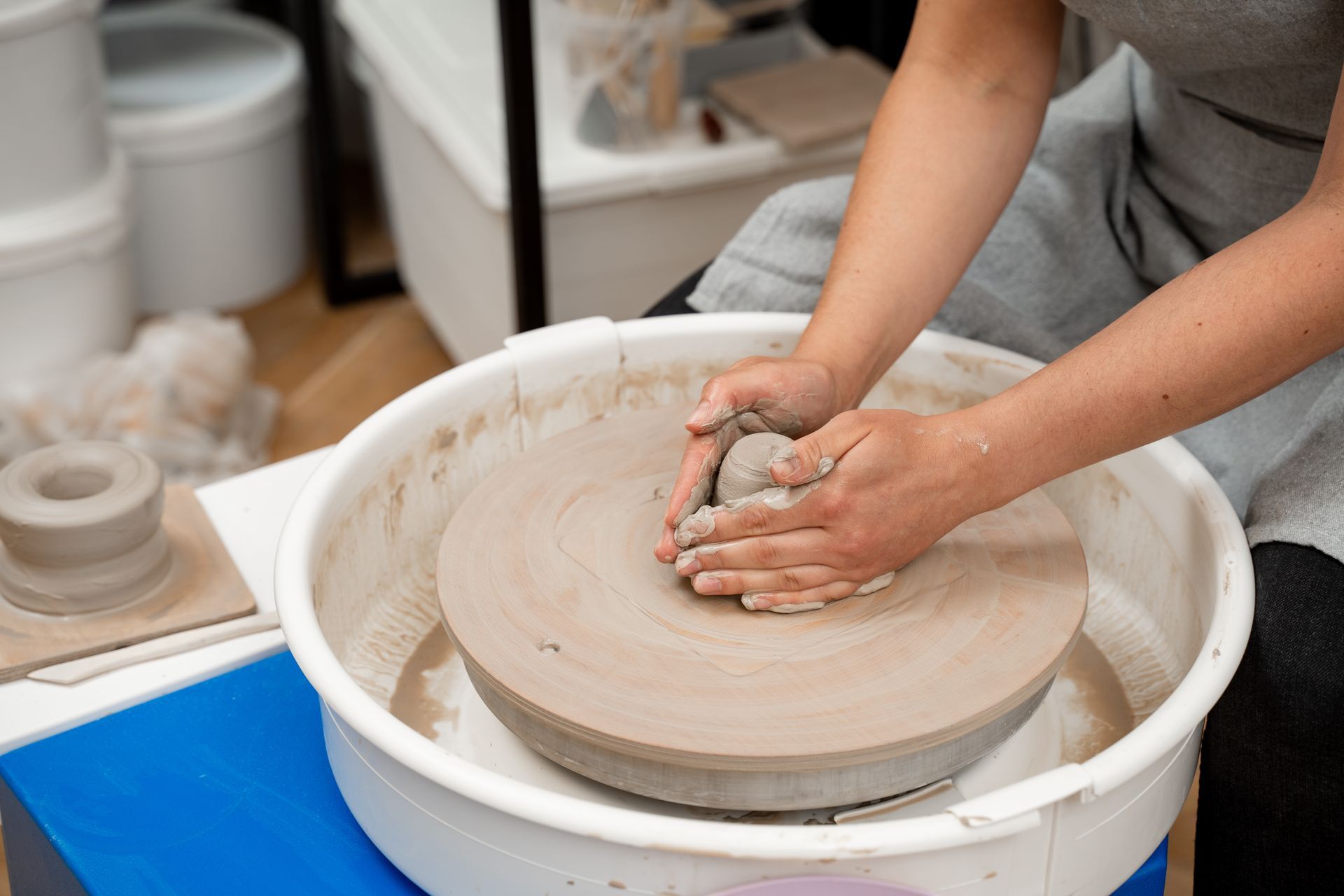 Person shaping clay on a pottery wheel; indoors, close-up on hands and wheel.