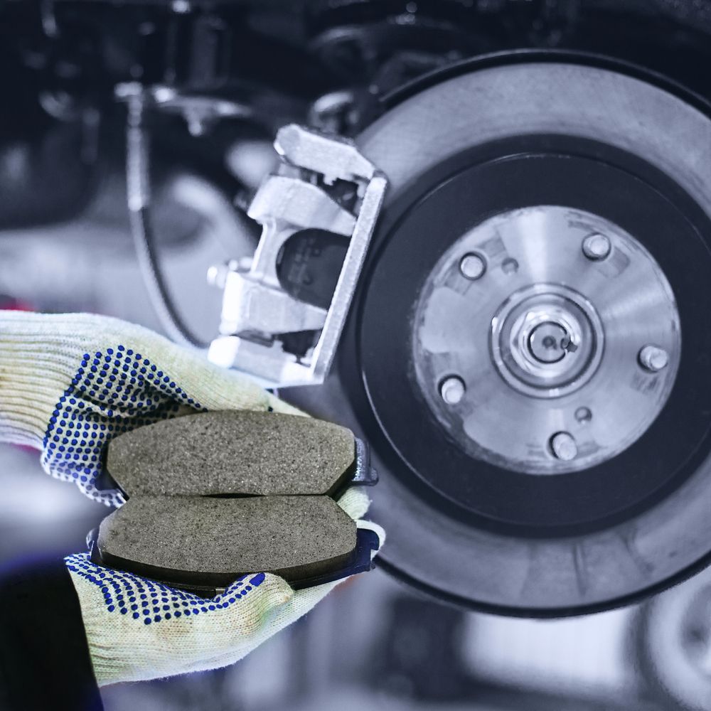 Una persona que lleva guantes sostiene pastillas de freno delante de la rueda de un automóvil.