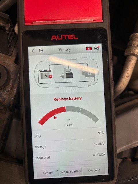 A handheld Autel battery tester shows a red