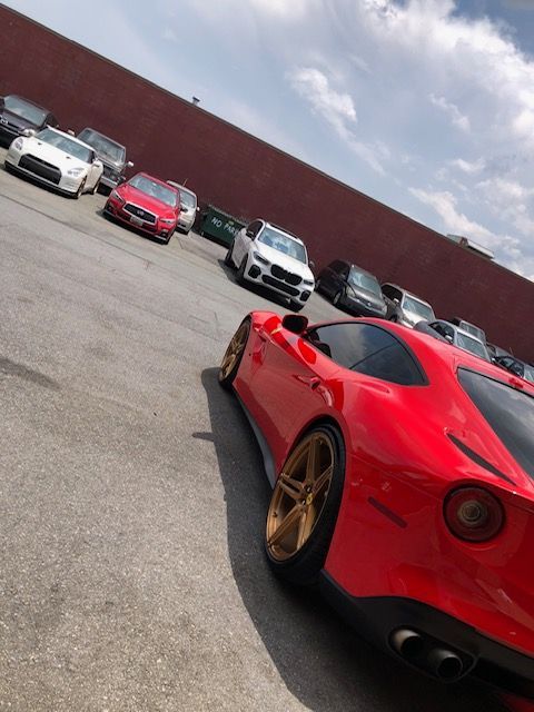 Red Ferrari sports car parked in a lot with other vehicles on a sunny day. | SB Automotive