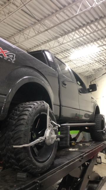 Black truck on a lift with alignment equipment attached to the front wheel. The setting is an auto shop. | SB Automotive