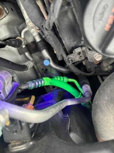 Green glowing AC lines in a car engine bay under a UV light, indicating a leak. | SB Automotive
