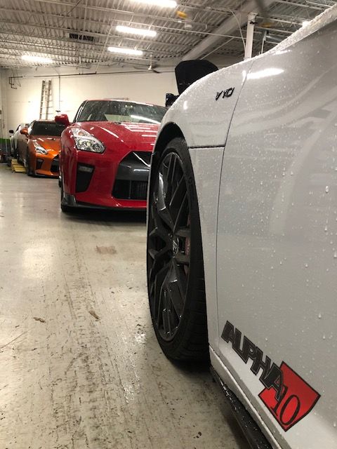 White car in garage, next to red car and orange car. Alpha 10 logo on side. | SB Automotive