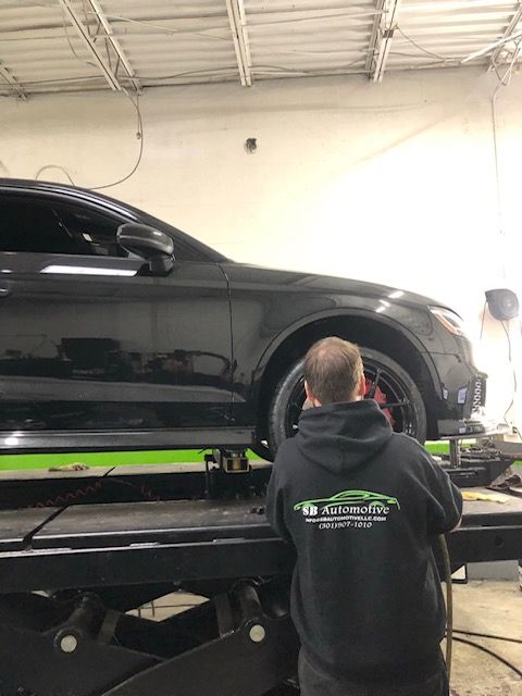 Man working on a black car raised on a lift in a garage. The man is wearing a black hoodie. | SB Automotive