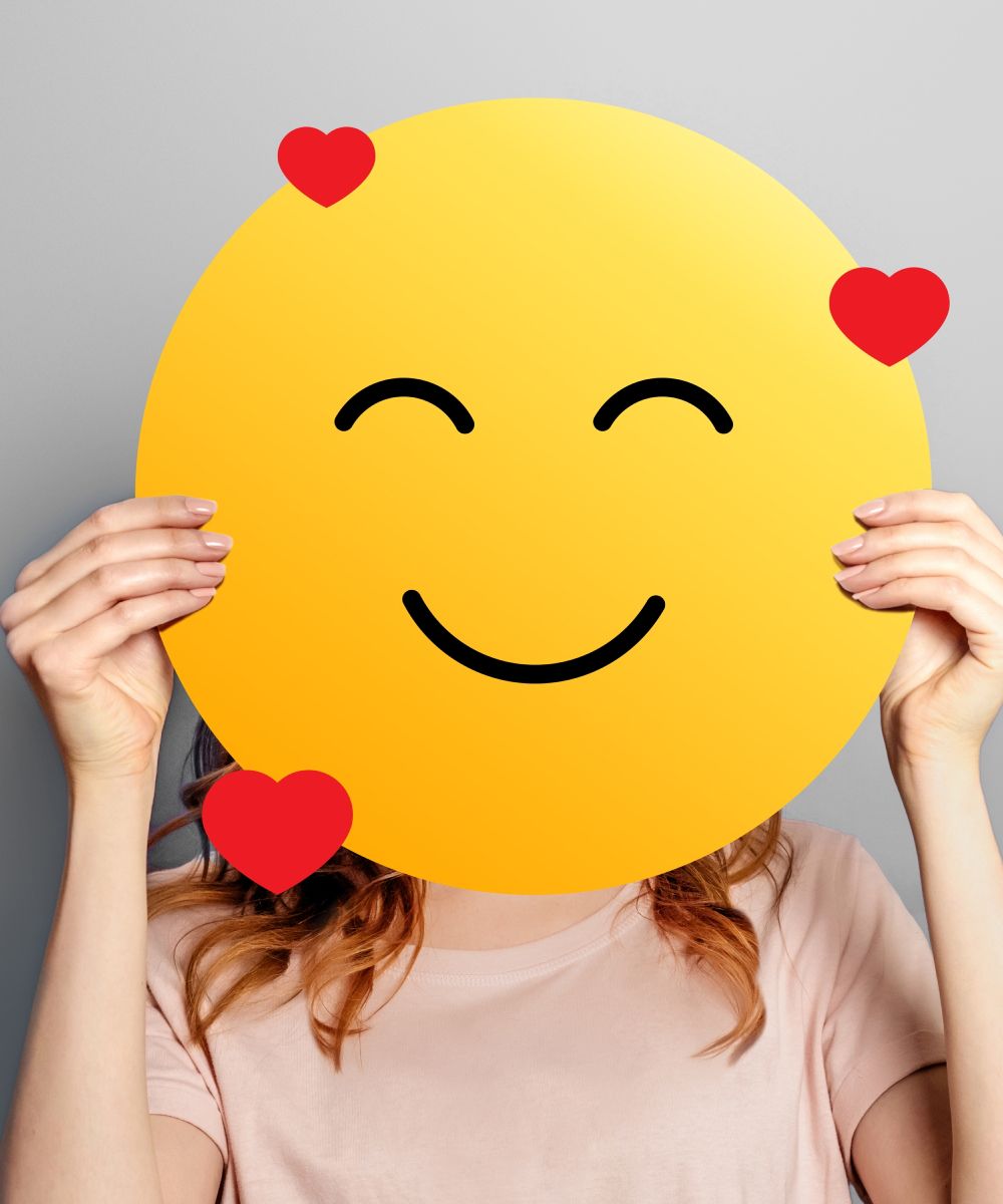 A woman is holding a smiley face with hearts around it