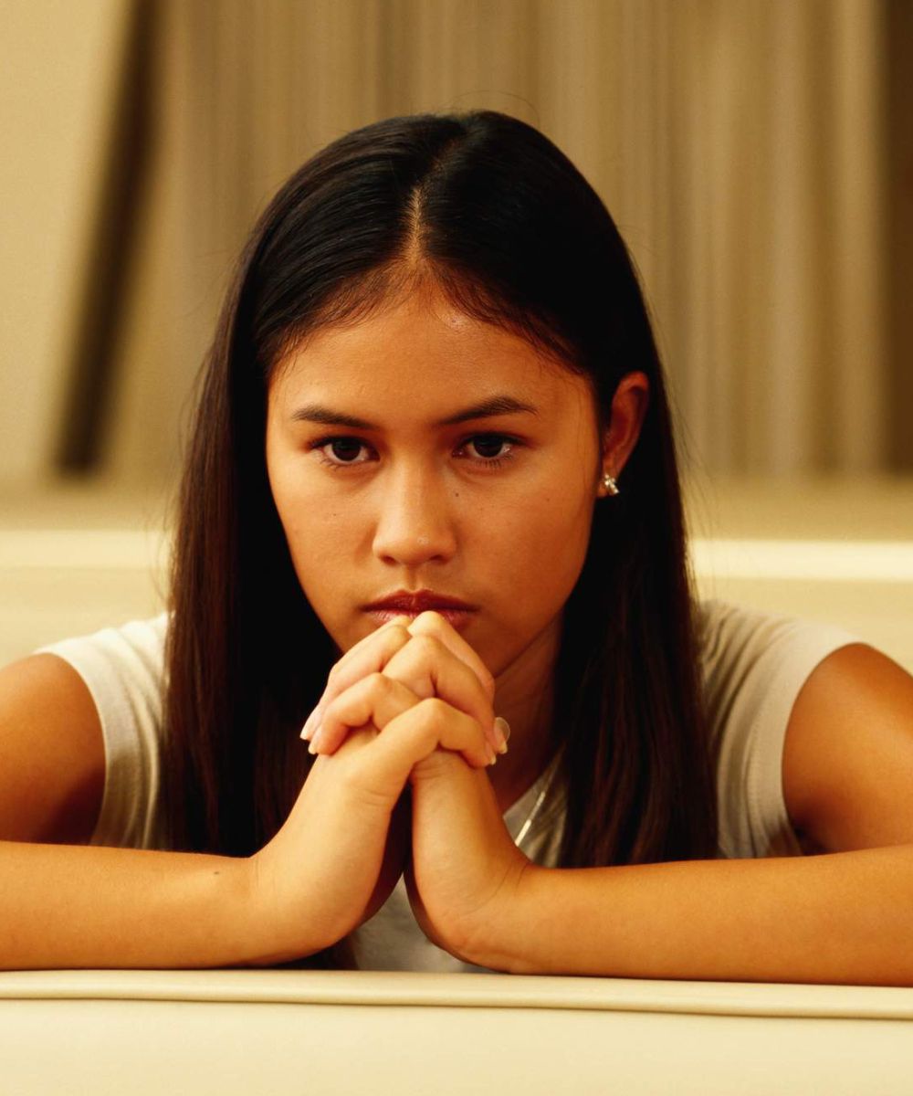 A woman with her hands folded looks at the camera