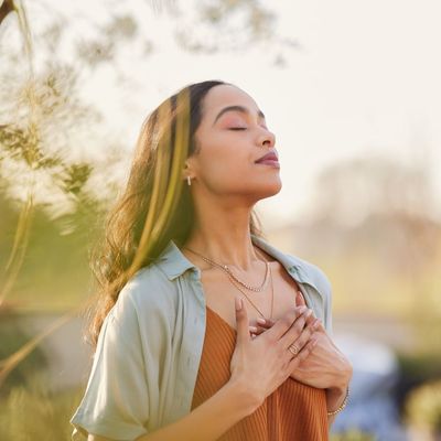 A woman is standing with her eyes closed and her hands on her chest.