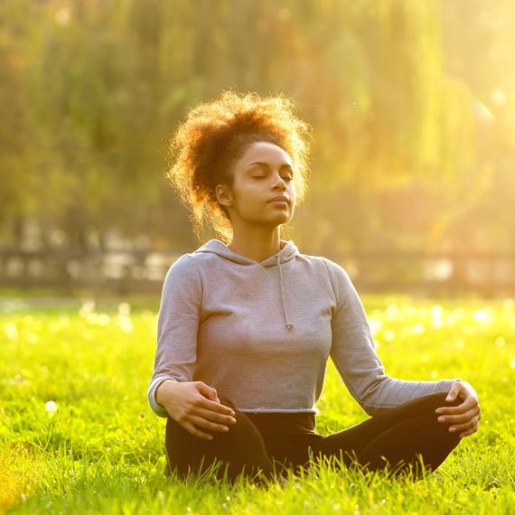 A woman is sitting in a lotus position in the grass with her eyes closed.