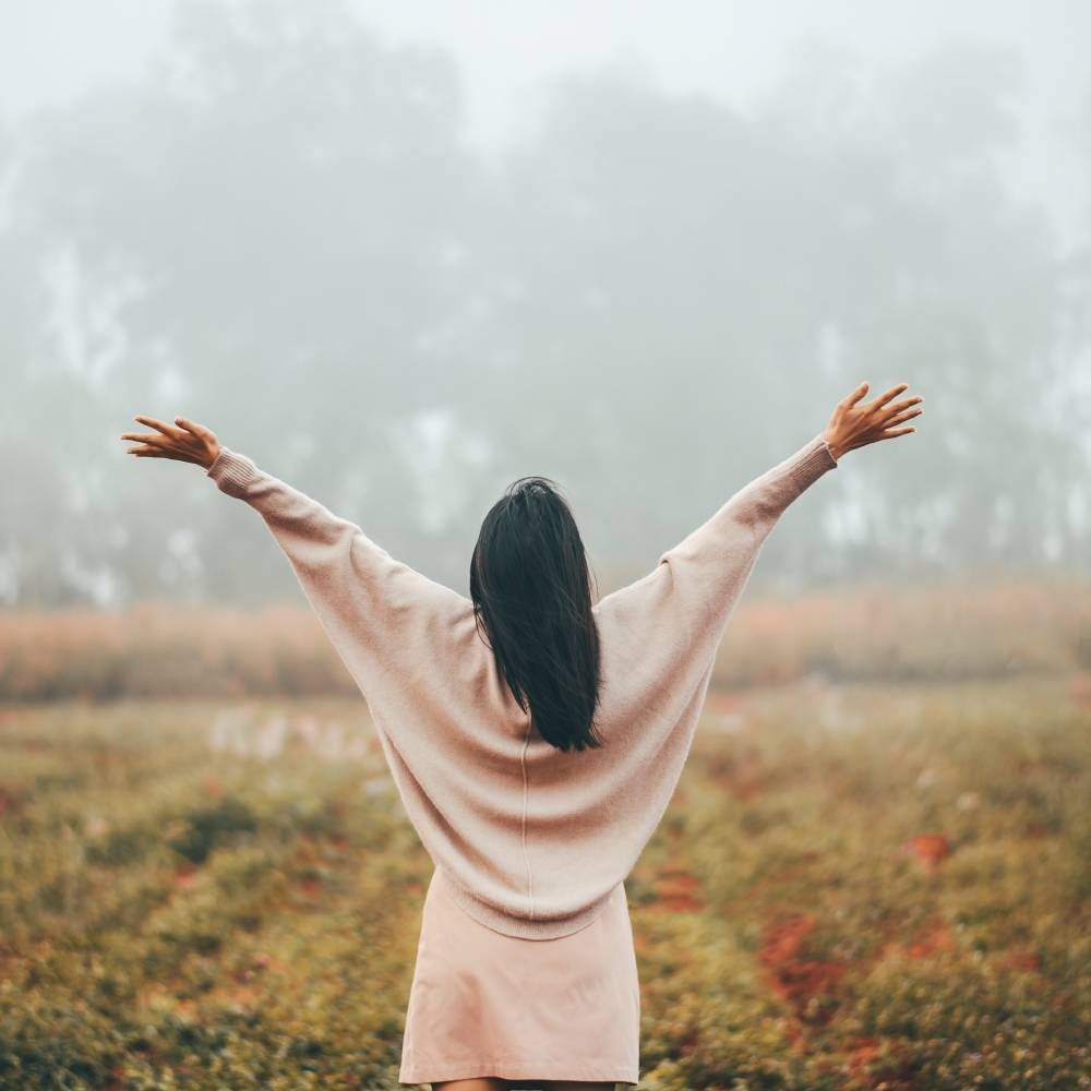 A woman is standing in a field with her arms outstretched.