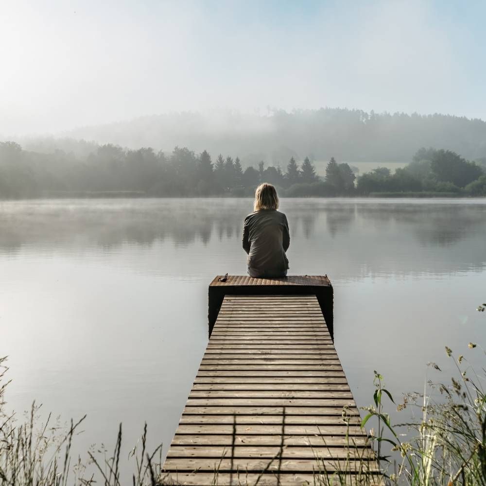 A woman is sitting on a dock overlooking a lake.