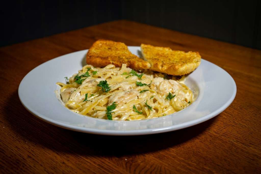 Fettucine Alfredo, Pasta dish with creamy sauce, garnished with parsley and two garlic bread slices on a white plate.