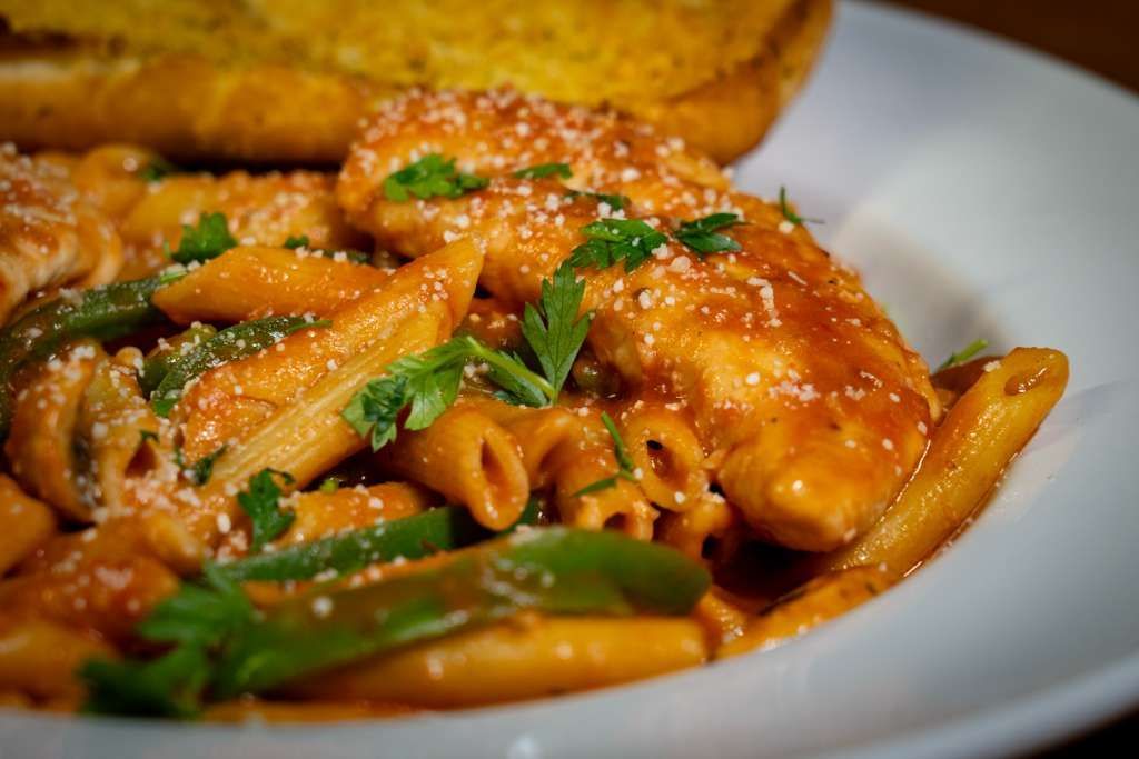 Penne pasta with chicken and green beans in a red sauce, topped with cheese and parsley, served with garlic bread.