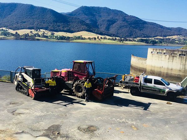 A group of trucks and tractors are parked next to a lake.