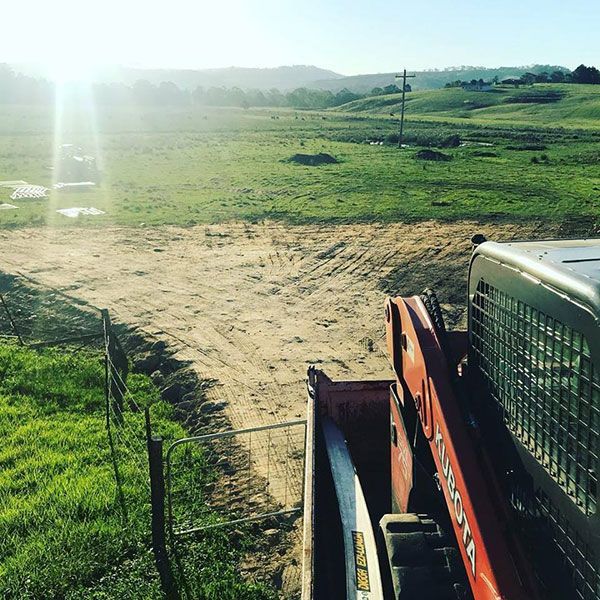 A tractor is driving down a dirt road in a field.
