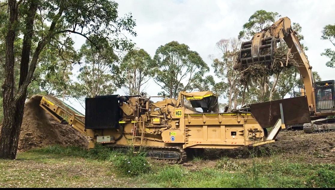A large yellow machine is sitting in the middle of a field next to a large excavator.