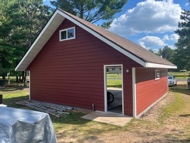 A red, single-story garage with white trim and a gabled roof set on a grassy, wooded lot.