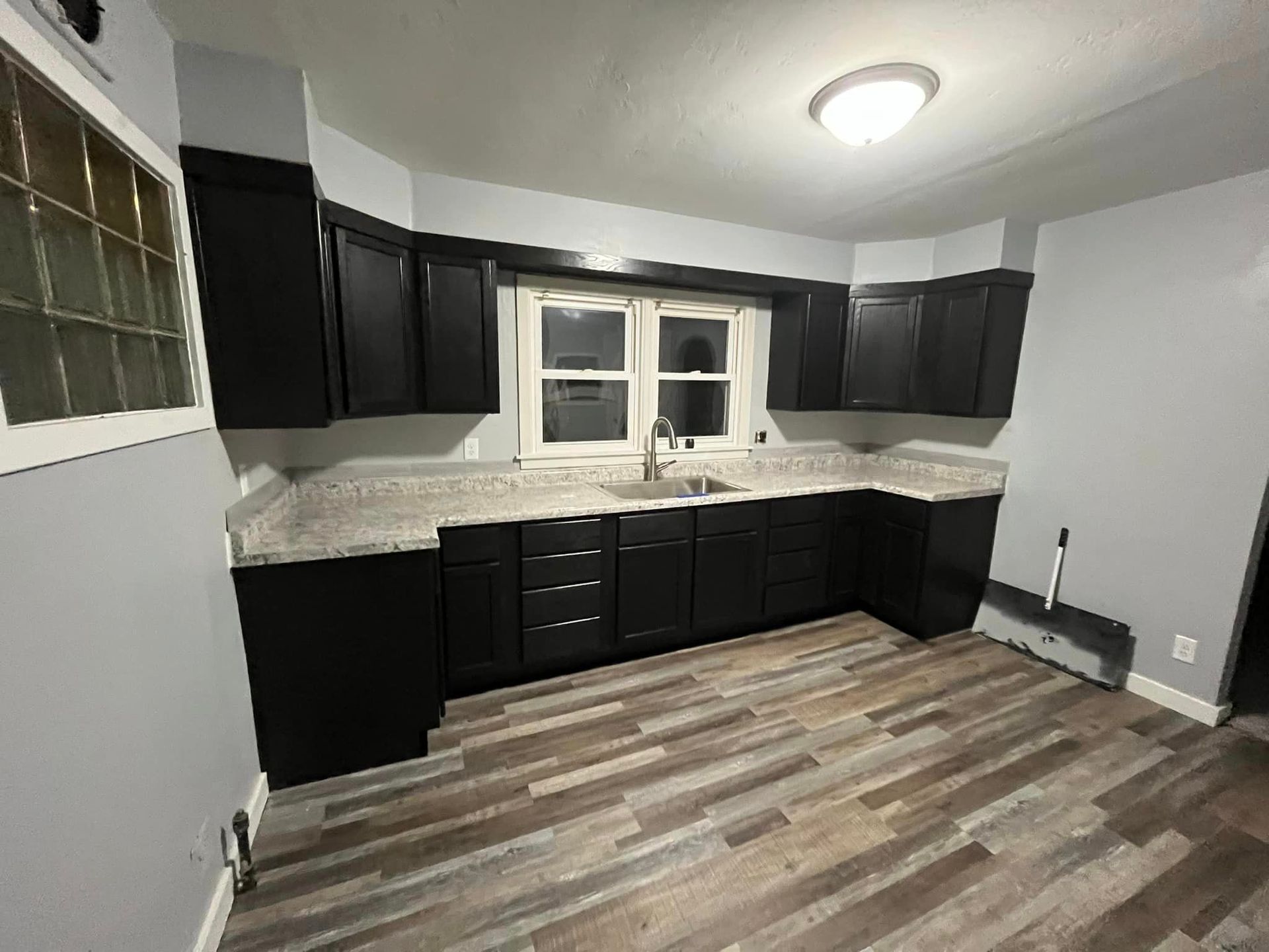 Kitchen with black cabinets, light granite countertops, grey walls, and wood-patterned vinyl flooring.