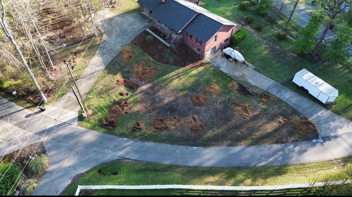 Overhead view of a house with a driveway and landscaping. Bare patches of land and a trailer are visible.