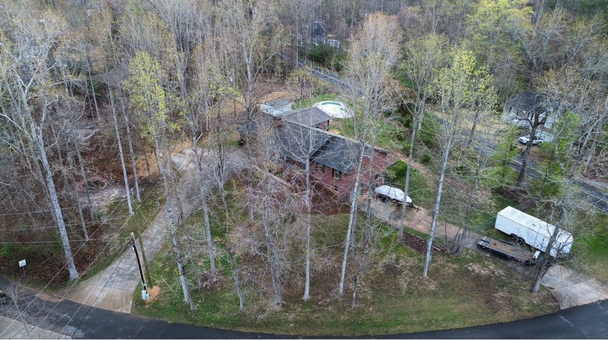 Aerial view of a house surrounded by trees with a trailer parked on the side and two driveways.