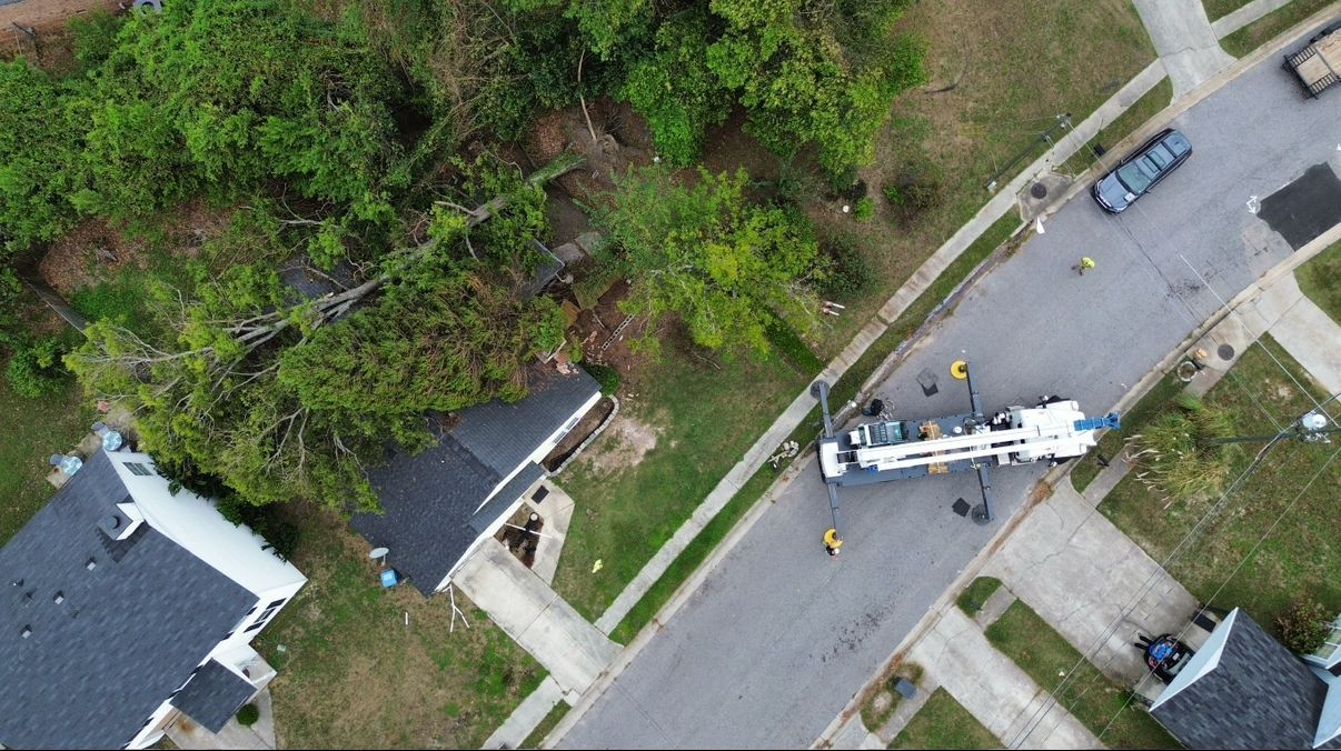 Aerial view of a street with a large truck, workers, and houses with green lawns and trees.