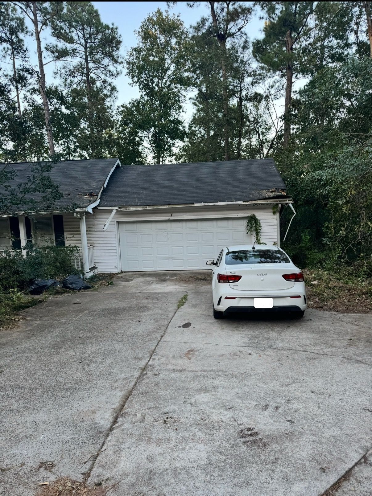 A white car parked in front of a white garage attached to a house.