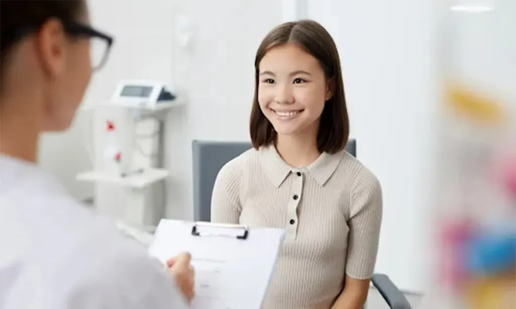 A young girl is sitting in a chair talking to a doctor.