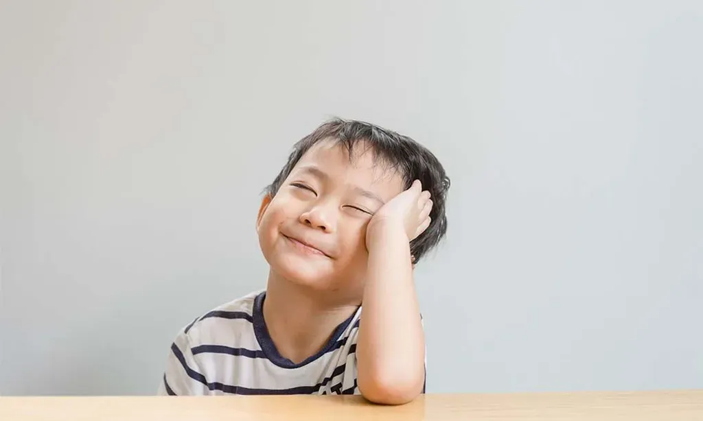 A young boy is sitting at a table with his hand on his head.