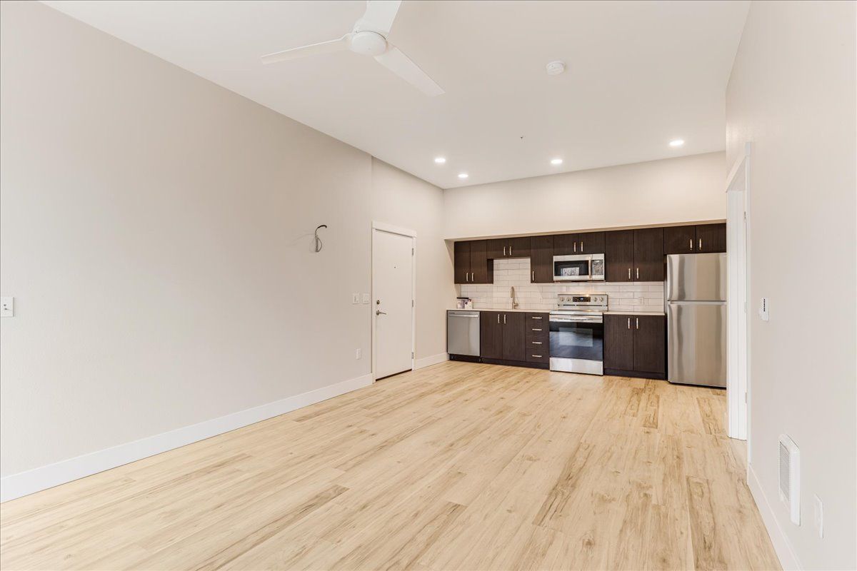 an empty living room with hardwood floors and a kitchen with stainless steel appliances .