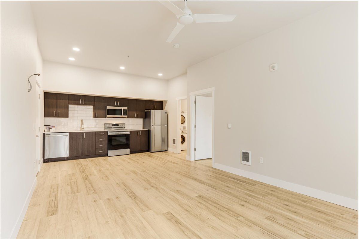 an empty living room with a kitchen and a ceiling fan .