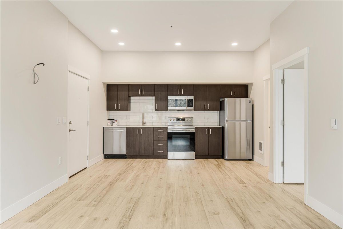 an empty kitchen with stainless steel appliances and wooden floors .