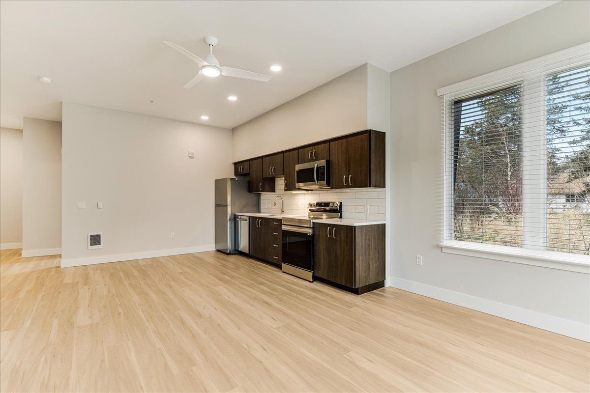an empty living room with a kitchen and a ceiling fan