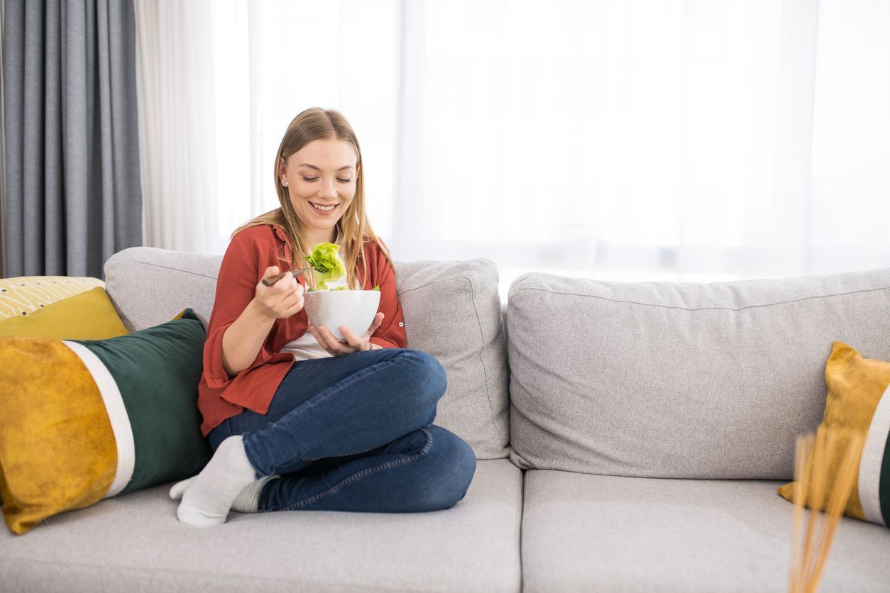 A young woman is sitting on the sofa, eating healthy food to stay healthy during fall and winter.